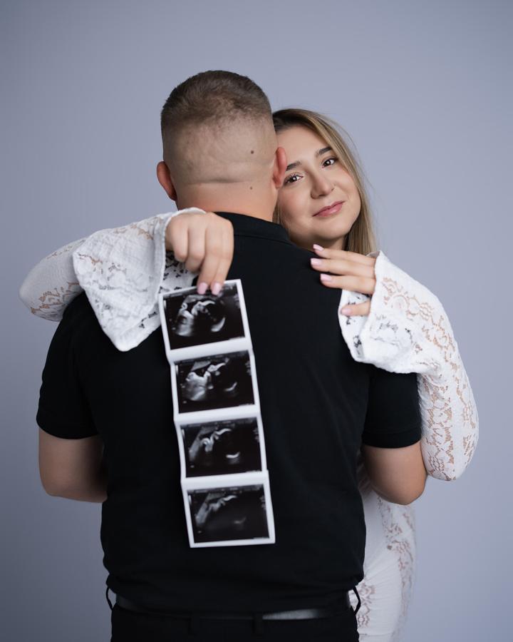 Para oczekująca dziecka pokazuje USG zdjęcia podczas sesji ciążowej na jednolitym tle.
