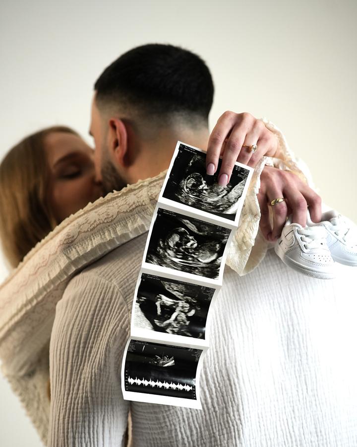 Pregnant couple holding ultrasound images with baby shoes, maternity session on neutral background.