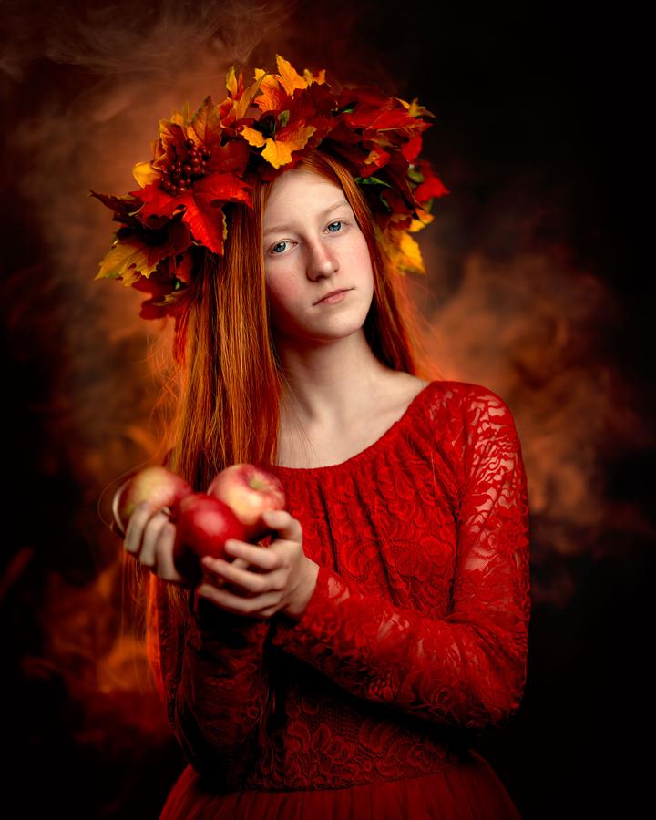 Dziewczyna z rudymi włosami w czerwonej koronacji jesiennej, trzymająca jabłka, sesja fine art.