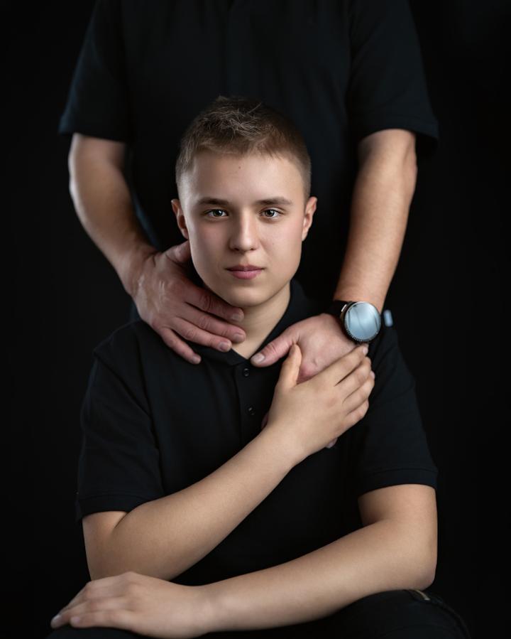 Chłopiec w czarnej koszulce z dorosłym na ciemnym tle, sesja rodzinna.