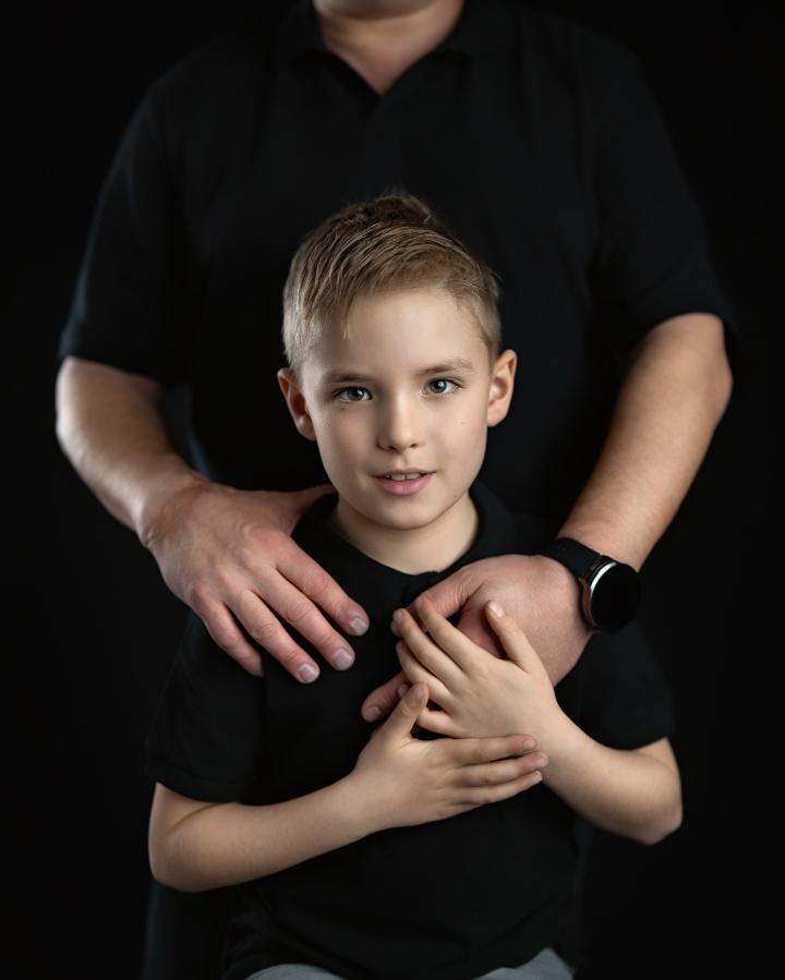 Boy in a black T-shirt embraced by a parent, dark background