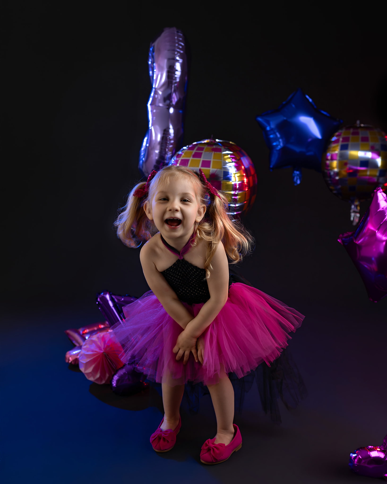 Lachend meisje in een roze tutu tussen kleurrijke ballonnen op een donkere achtergrond
