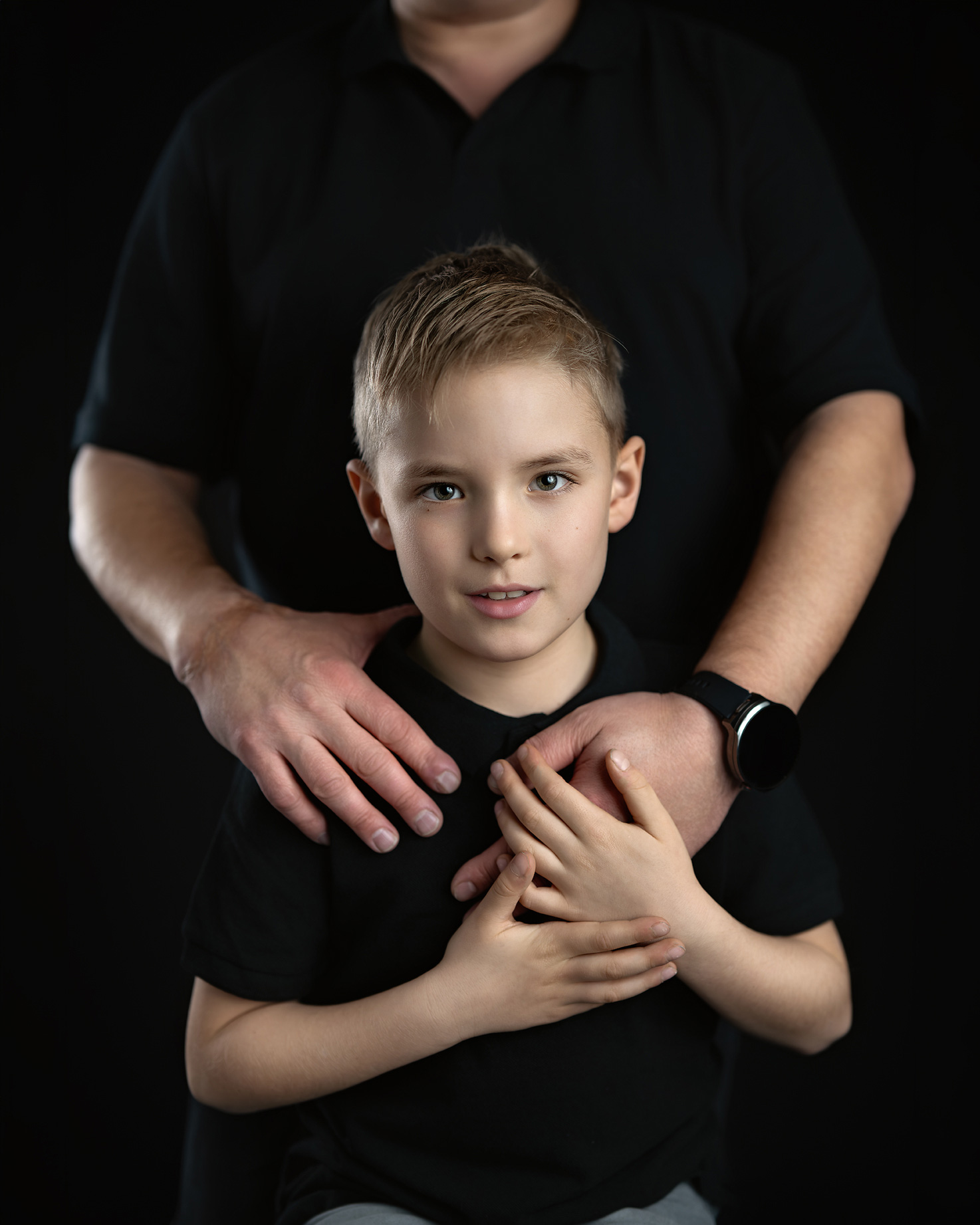 Jongen in een zwart T-shirt in de armen van een ouder, donkere achtergrond